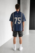 Homme portant un maillot bleu marine bonhomme avec le numéro 75 et des motifs parisiens au dos, coupe oversize.